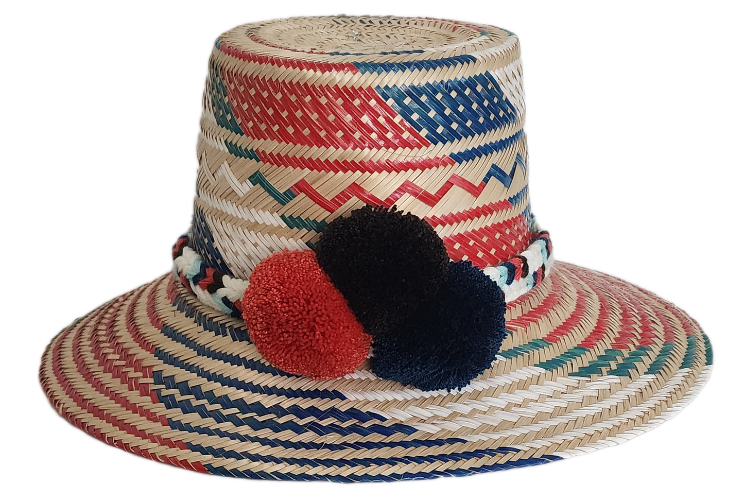 Boho Wayuu straw hat featuring vibrant red, navy, and green woven patterns, a hand-braided multicolor band, and bold red and black pom-poms — a colorful, handcrafted bohemian accessory perfect for summer.