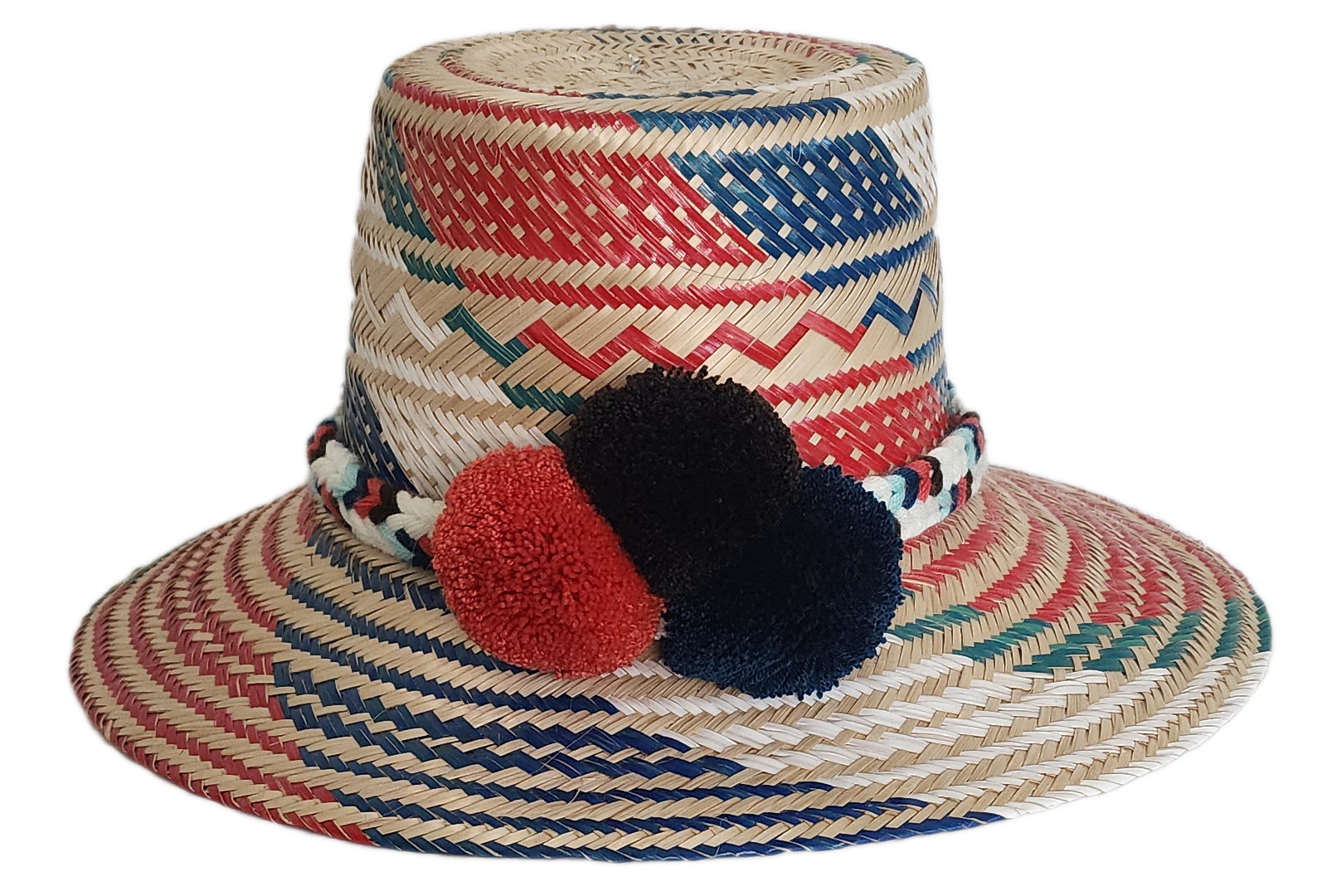 Boho Wayuu straw hat featuring vibrant red, navy, and green woven patterns, a hand-braided multicolor band, and bold red and black pom-poms — a colorful, handcrafted bohemian accessory perfect for summer.