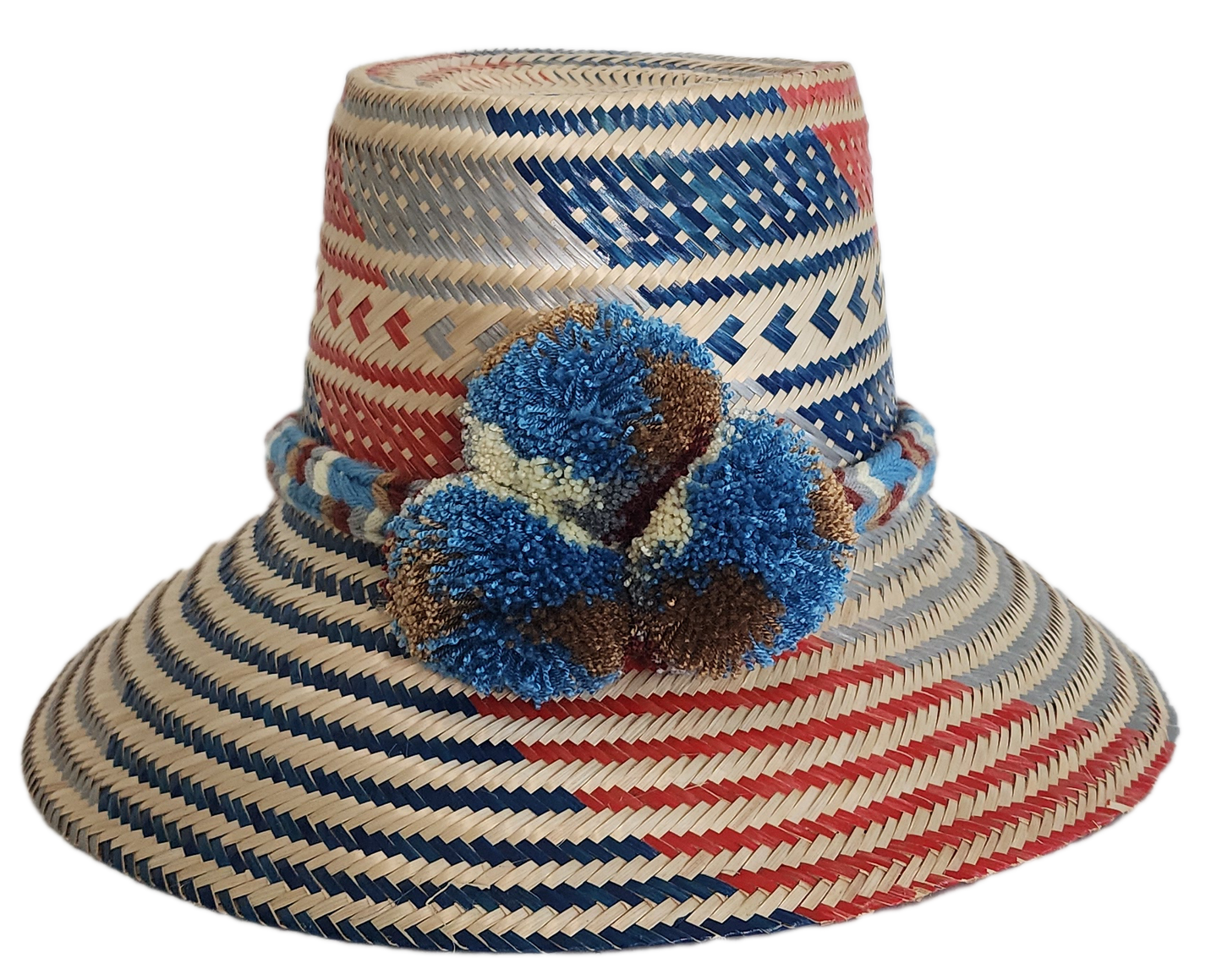 Colorful boho straw hat handmade by Wayuu artisans, featuring red, blue, and natural woven patterns with bold blue pom-poms — a vibrant bohemian accessory perfect for summer style