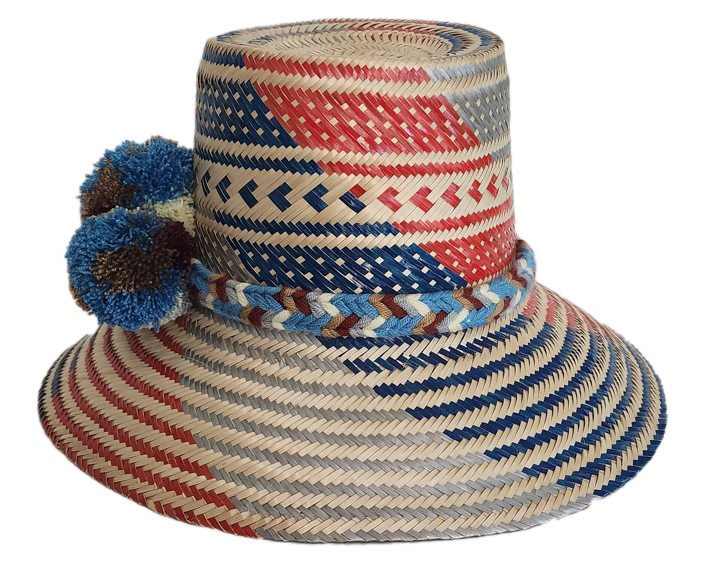 Colorful boho straw hat handmade by Wayuu artisans, featuring red, blue, and natural woven patterns with bold blue pom-poms — a vibrant bohemian accessory perfect for summer style