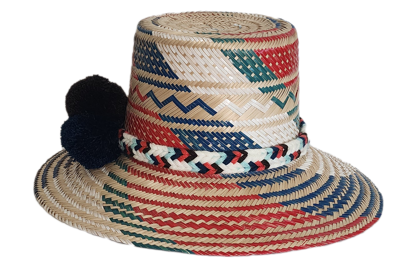 Boho Wayuu straw hat featuring vibrant red, navy, and green woven patterns, a hand-braided multicolor band, and bold red and black pom-poms — a colorful, handcrafted bohemian accessory perfect for summer.