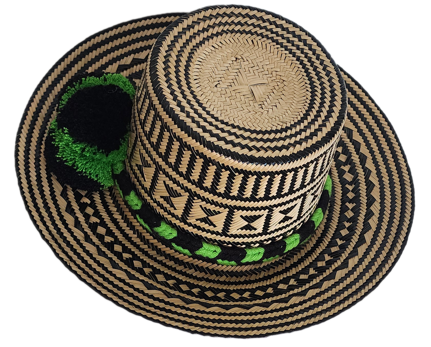 Handcrafted Wayuu straw hat with bold black geometric patterns, natural beige base, a wide circular brim, and a black and green pom-pom band accent.