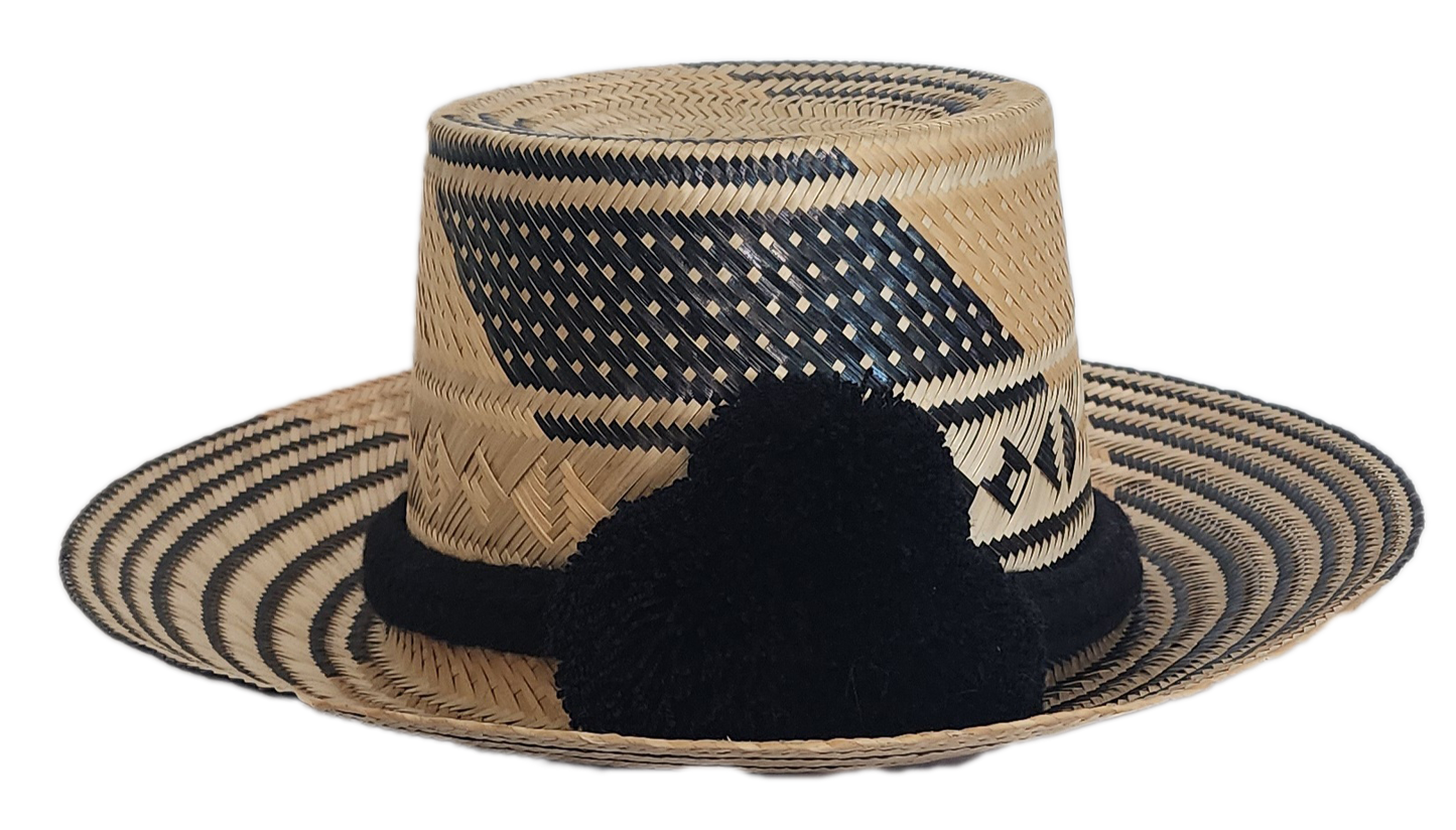 A stylish, handmade straw hat featuring intricate black and natural straw weaving patterns and a bold black pompom band.