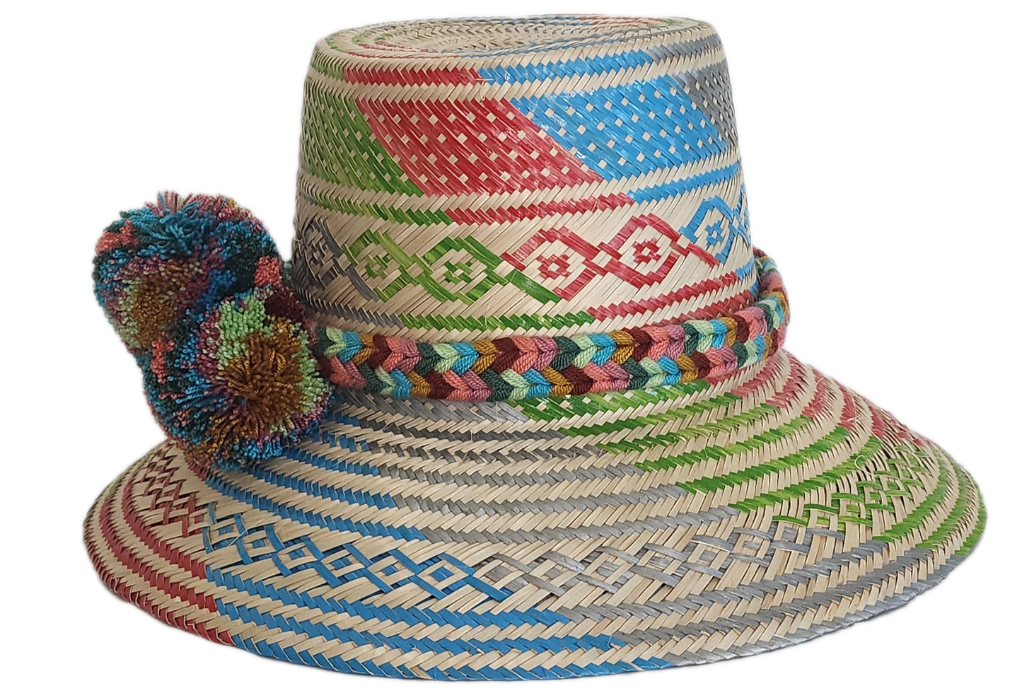 A vibrant, handmade straw hat featuring a patchwork of colorful geometric patterns in red, green, blue, and grey, and a multicolored pompom band with orange, blue, and red.