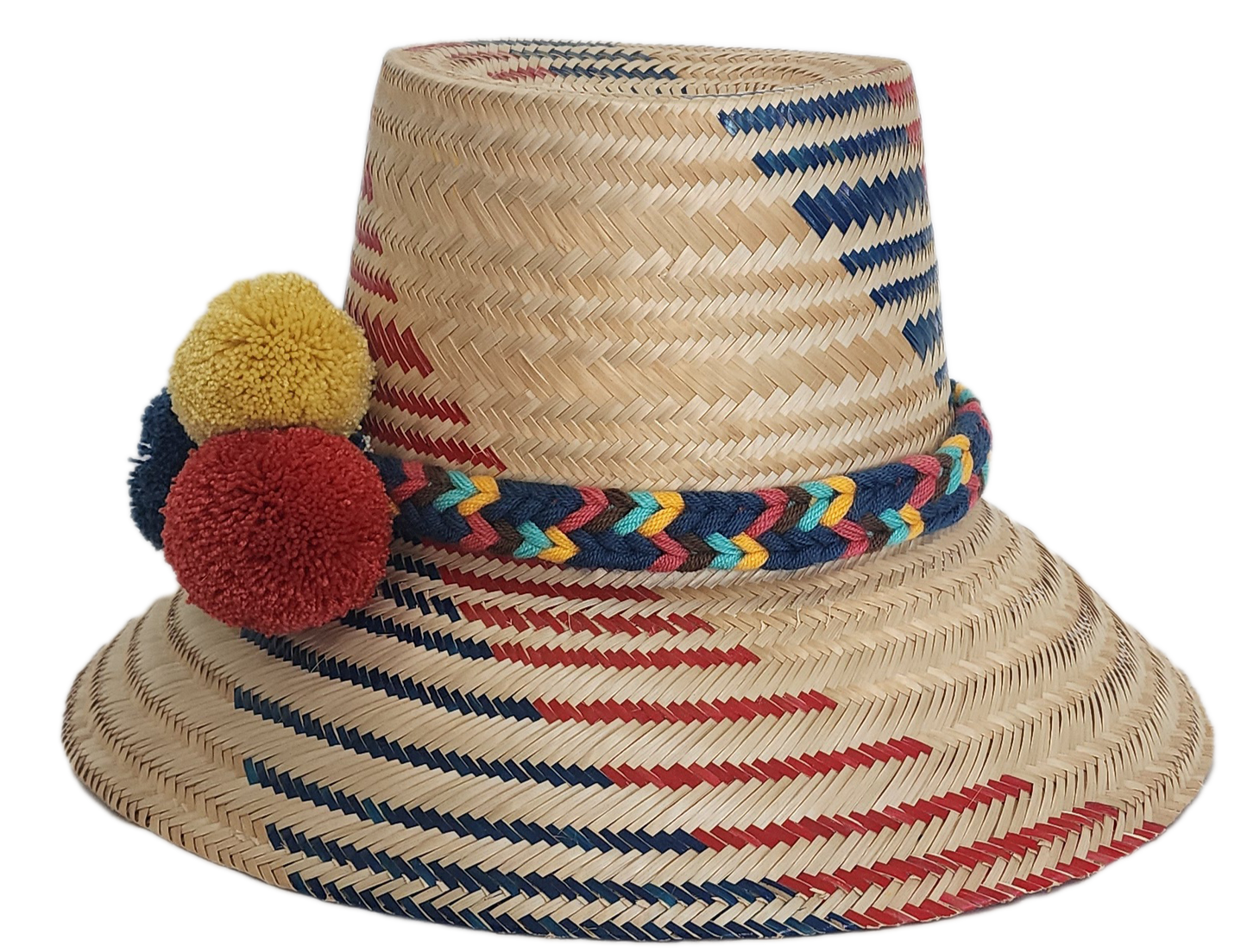 A vibrant, handmade straw hat featuring red and blue geometric patterns on a natural straw base and a colorful pompom band with yellow, dark blue, and red pompoms.