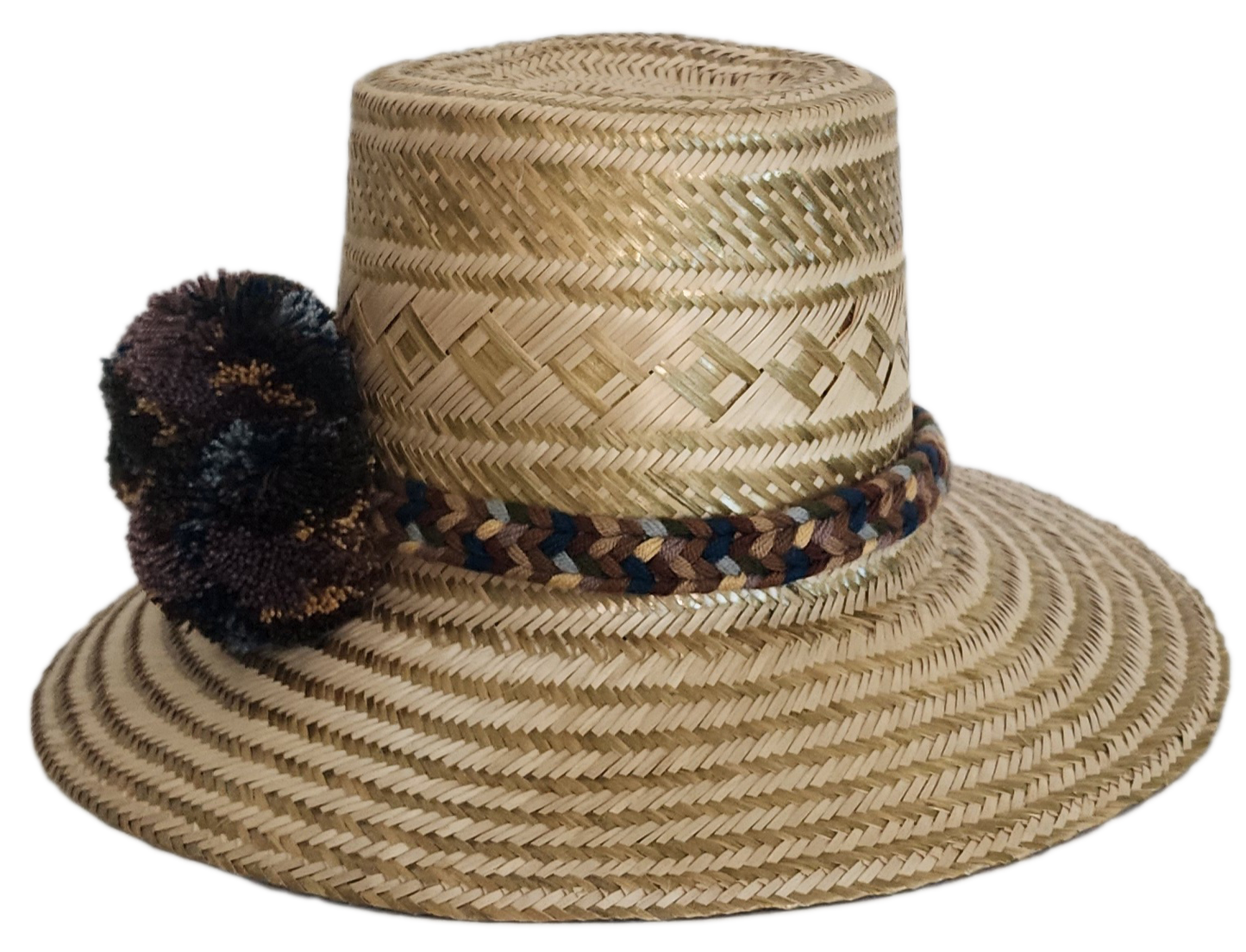 A stylish, handmade straw hat featuring subtle geometric patterns in natural and darker straw, accented by a textured band with brown, blue, and cream elements and a dark, multicolored pompom.