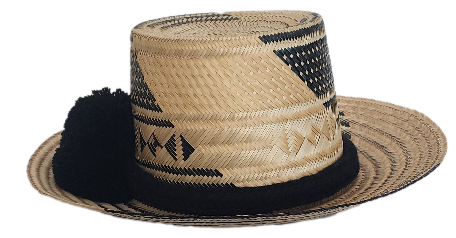A stylish, handmade straw hat featuring intricate black and natural straw weaving patterns and a bold black pompom band.