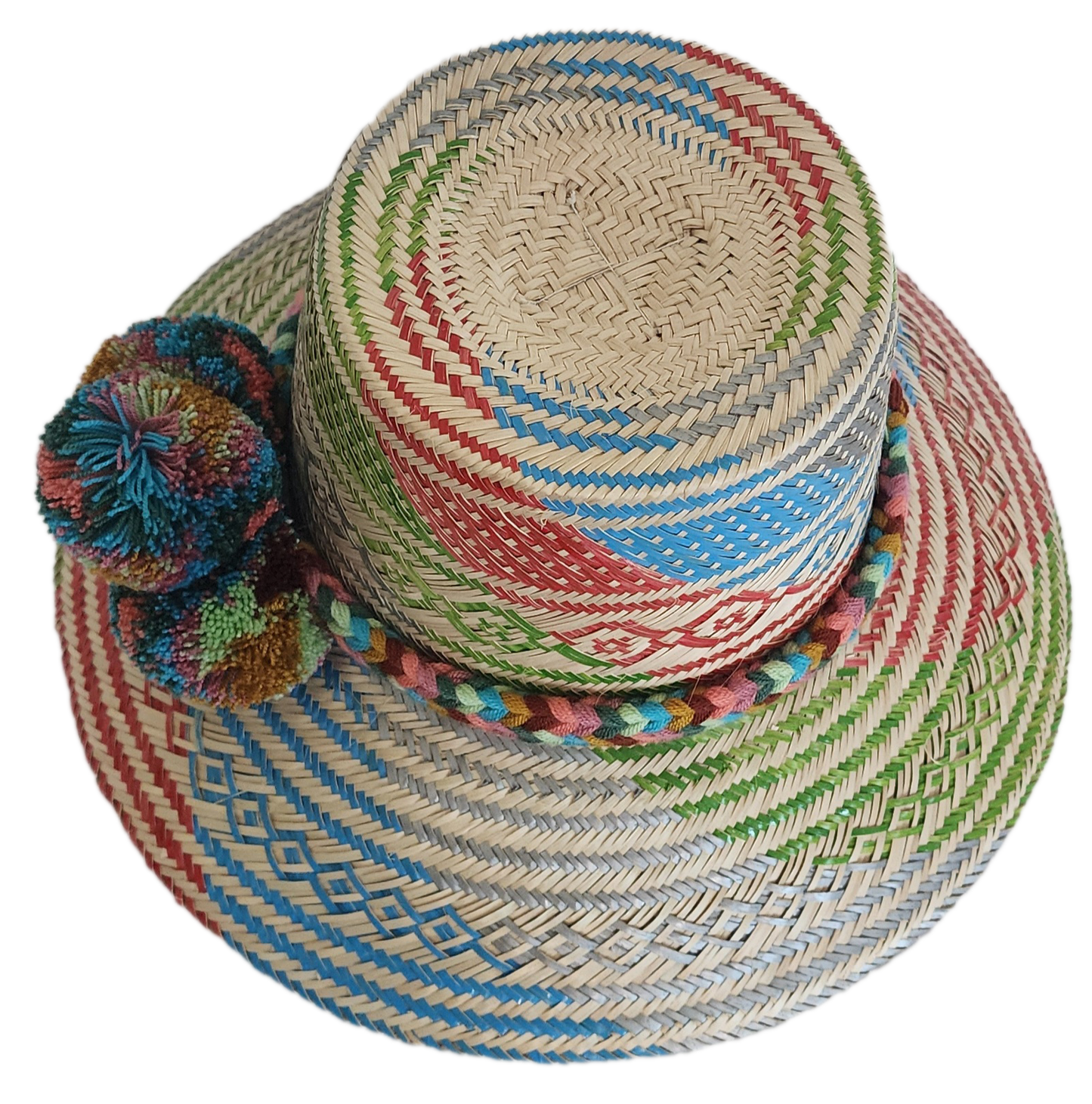A vibrant, handmade straw hat featuring a patchwork of colorful geometric patterns in red, green, blue, and grey, and a multicolored pompom band with orange, blue, and red.