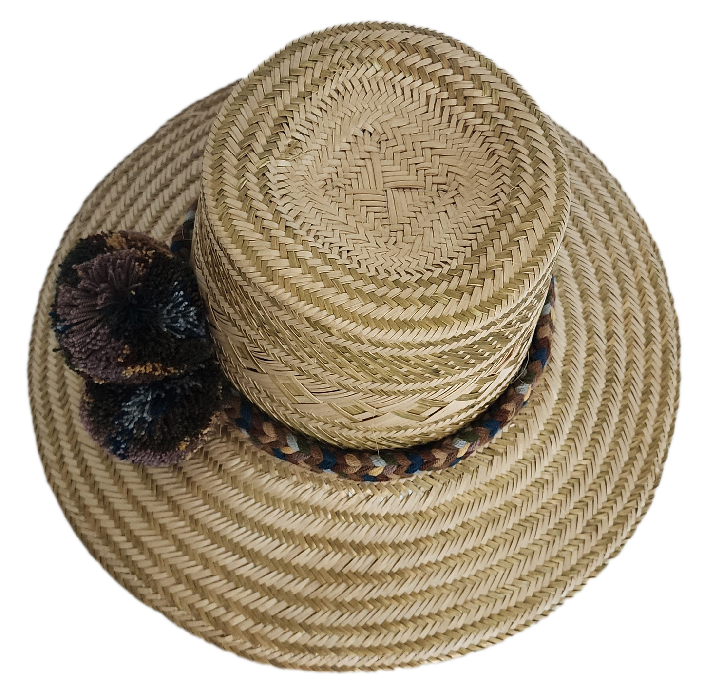 A stylish, handmade straw hat featuring subtle geometric patterns in natural and darker straw, accented by a textured band with brown, blue, and cream elements and a dark, multicolored pompom.