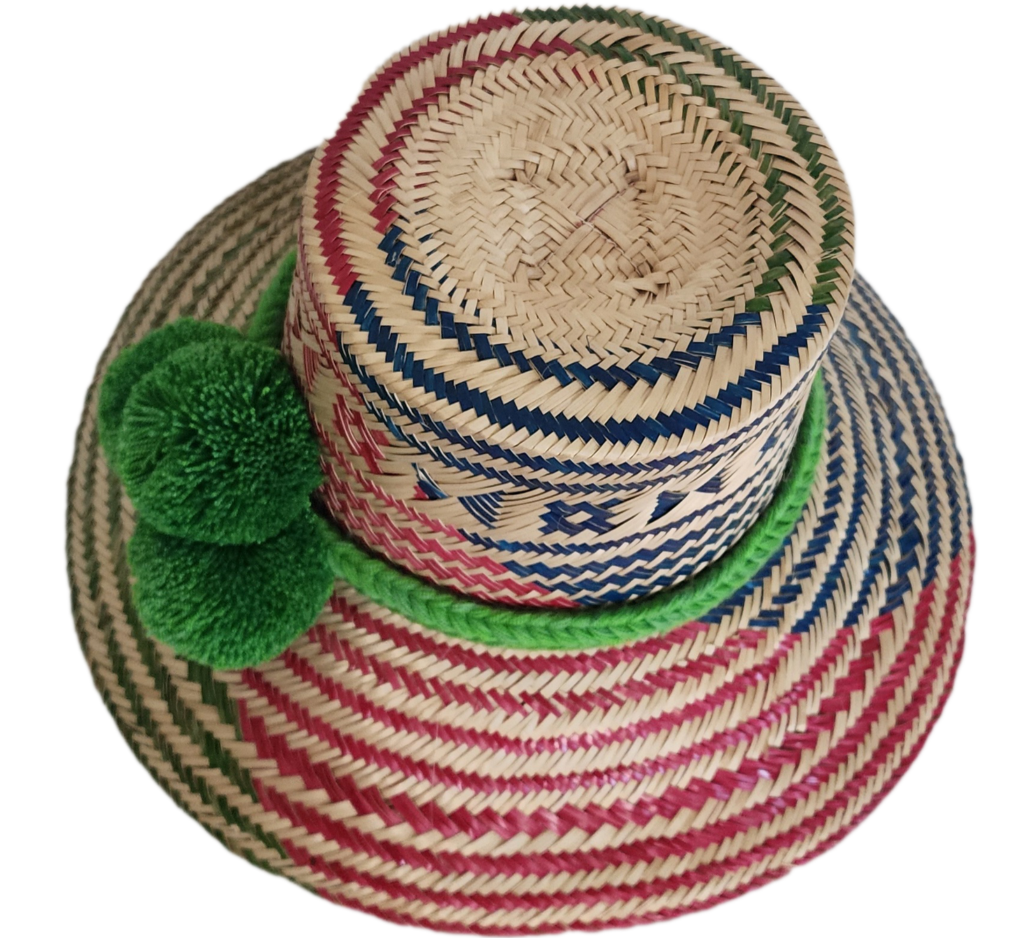 A colorful, handmade straw hat with red, blue, and green geometric patterns and a vibrant green pompom band with three fluffy pompoms.