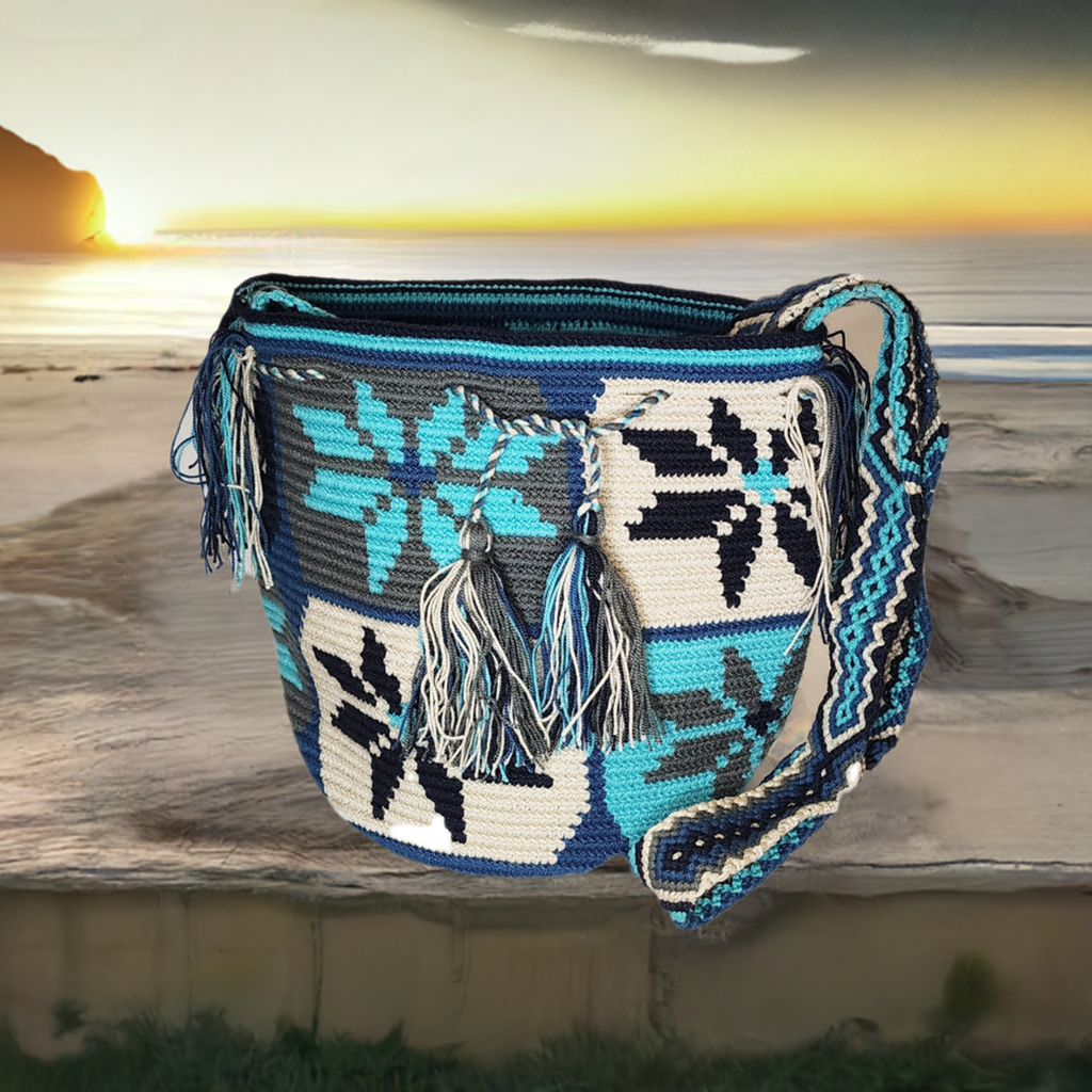 Boho chick Wayuu crochet bag in blue, white, and black with floral motifs and tassels, handmade by Wayuu artisans.