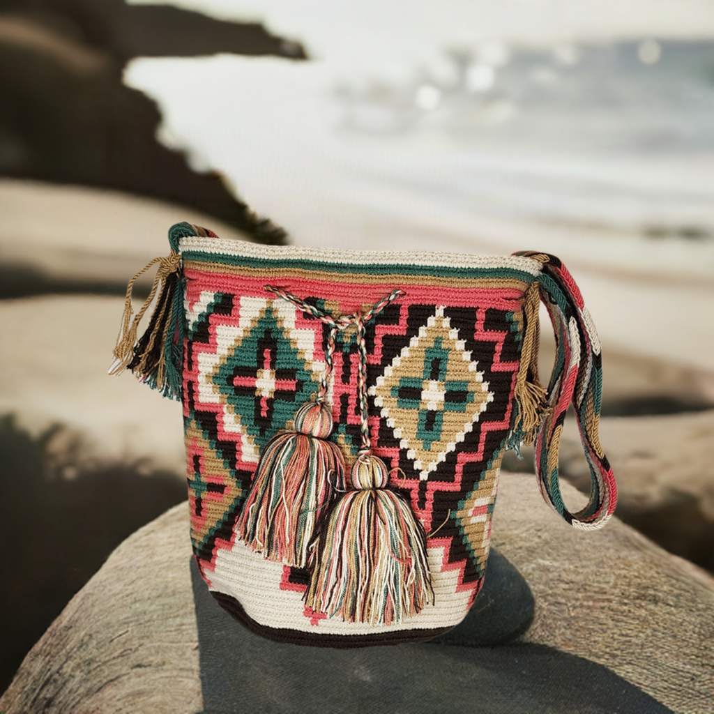 Handmade bohemian Wayuu crochet bag with tribal diamond patterns in burgundy, cream, forest green, and brown. Features long strap and tassel drawstring.