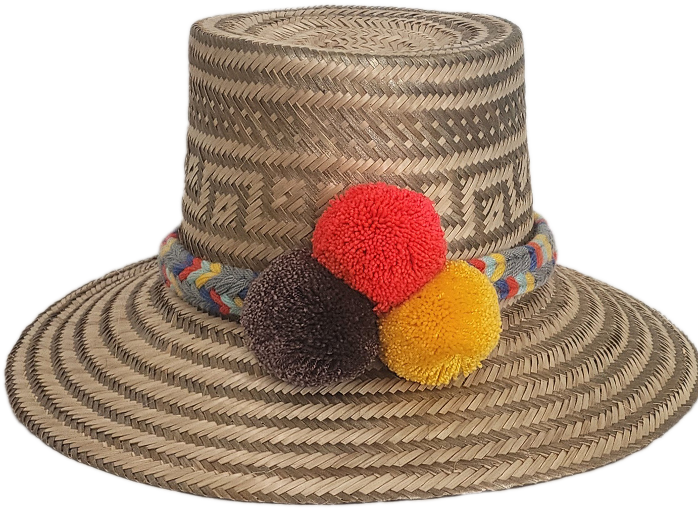 Handwoven Wayuu straw hat with intricate gray-beige tribal patterns, a colorful braided band, and red, yellow, and dark brown pom-poms. Artisan boho style.