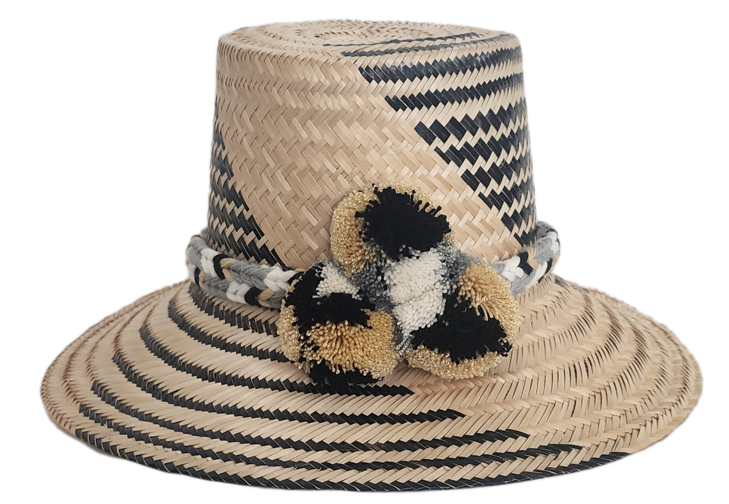 Handwoven Wayuu straw hat with black zigzag pattern, wide brim, and braided band featuring neutral-toned pom-poms. A modern boho-chic artisan accessory.