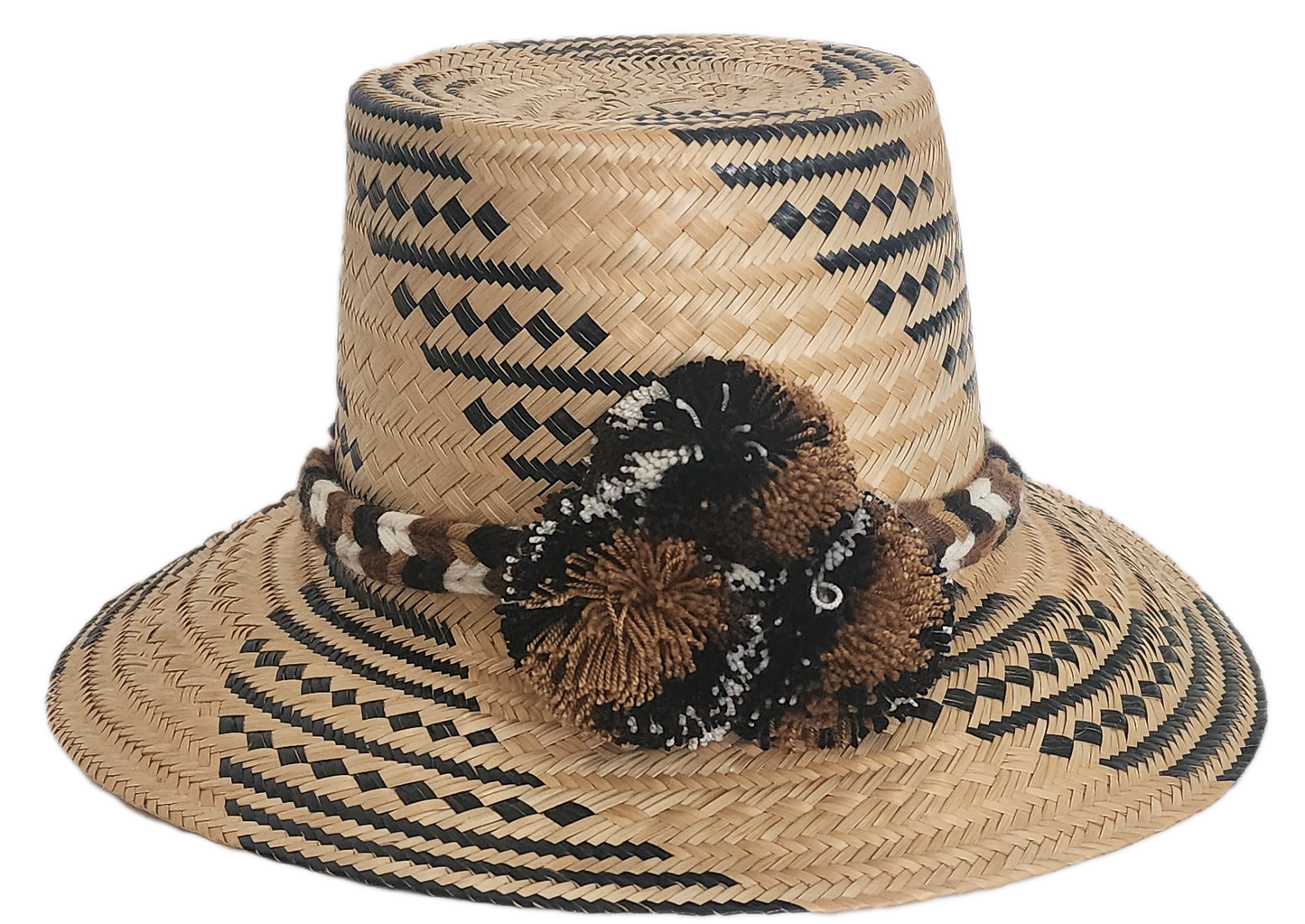 Handwoven Wayuu straw hat with black and brown geometric patterns, a braided band, and matching pom-poms. A rich, artisan-crafted boho accessory.