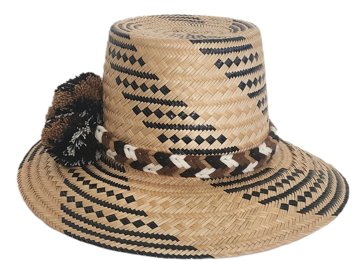 Handwoven Wayuu straw hat with black and brown geometric patterns, a braided band, and matching pom-poms. A rich, artisan-crafted boho accessory.