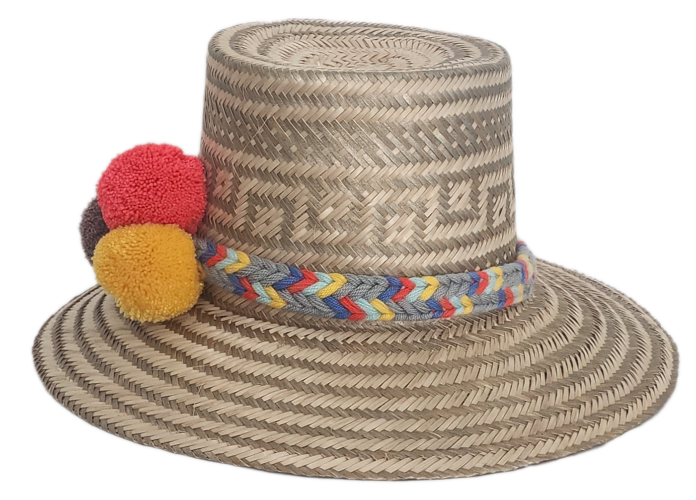 Handwoven Wayuu straw hat with intricate gray-beige tribal patterns, a colorful braided band, and red, yellow, and dark brown pom-poms. Artisan boho style.