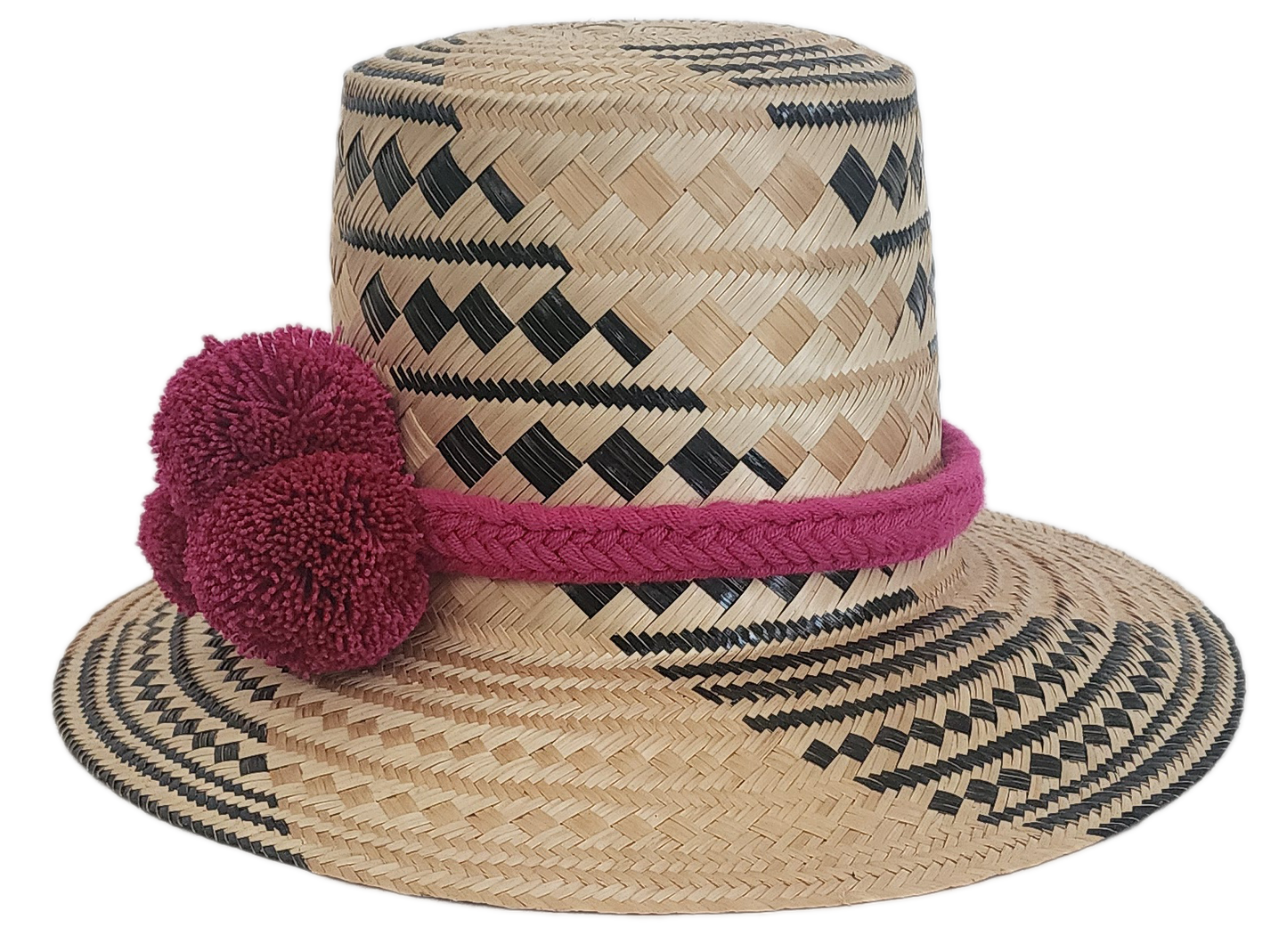 Handwoven Wayuu hat with deep pink pom-poms, braided band, and black geometric details on straw.