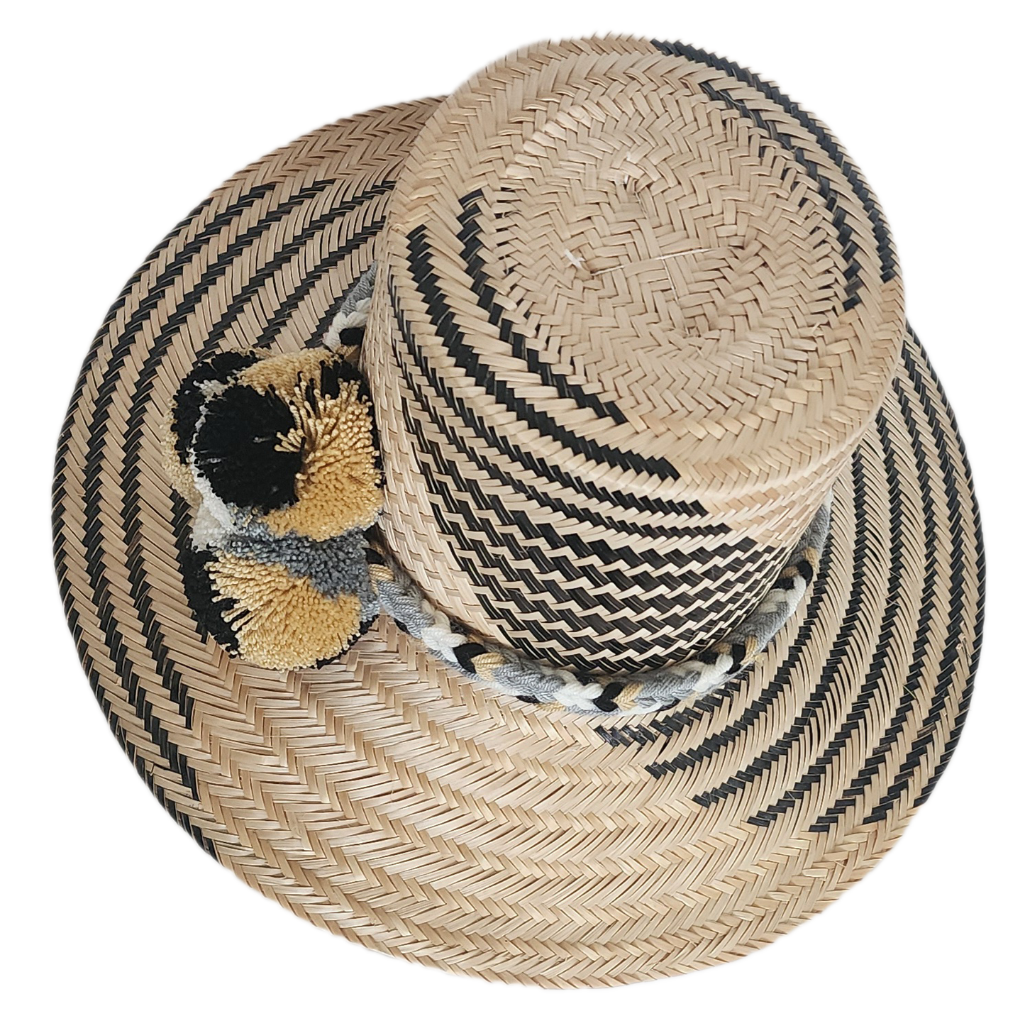 Handwoven Wayuu straw hat with black zigzag pattern, wide brim, and braided band featuring neutral-toned pom-poms. A modern boho-chic artisan accessory.
