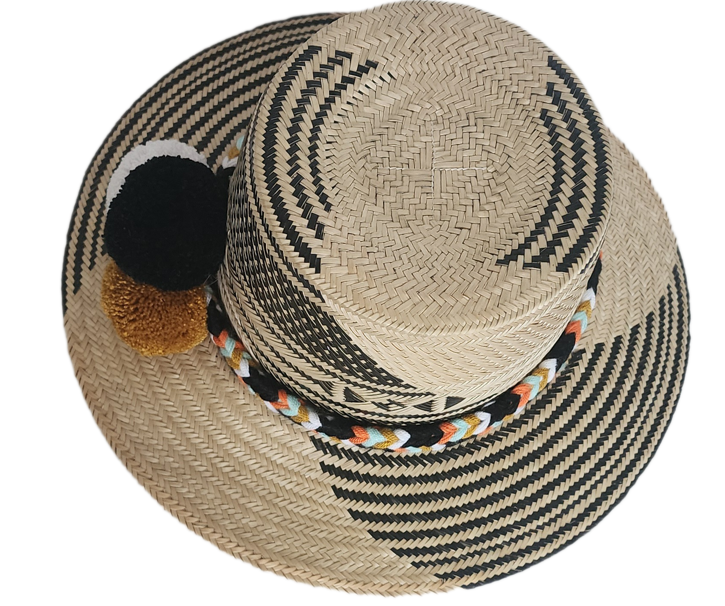 Handwoven Wayuu straw hat with bold black diagonal weave, a colorful braided band, and black, white, and mustard pom-poms. A refined boho fashion piece.