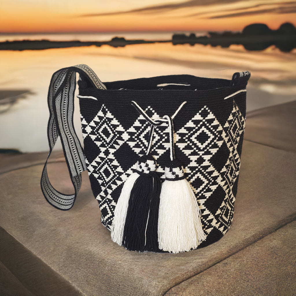 Handmade Wayuu crochet bag in black and white with diamond geometric patterns, large black and white tassels, and artisan-crafted crossbody strap.