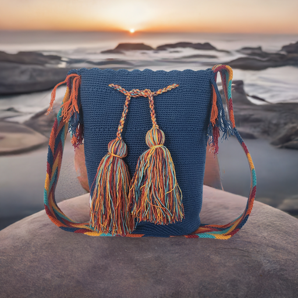 Handmade Wayuu crochet bag with navy blue body, multicolor strap, and large vibrant tassels, artisan-crafted crossbody style.