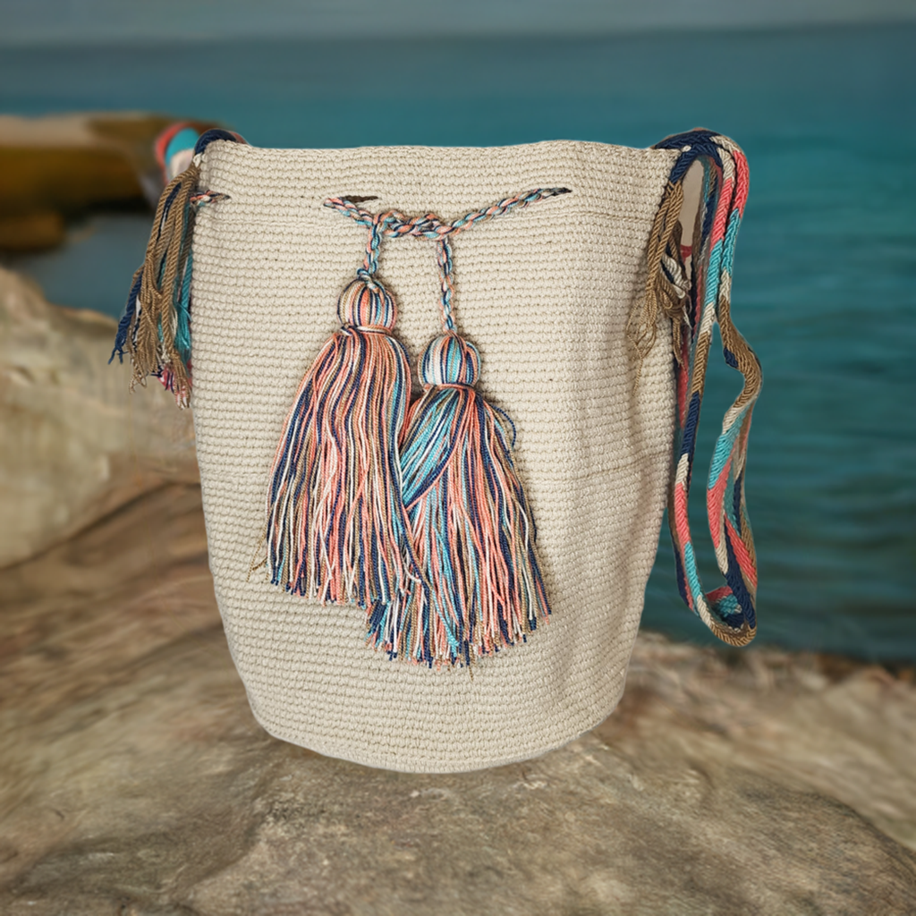 Handmade Wayuu crochet bag in cream with oversized multicolor tassels, artisan-crafted with a vibrant patterned crossbody strap.