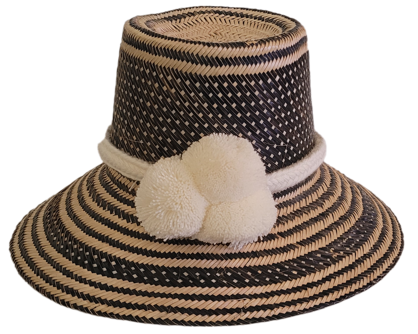 Boho handmade Wayuu hat in black and natural tones with ivory white pompoms and woven geometric patterns — artisan-crafted straw hat for women.