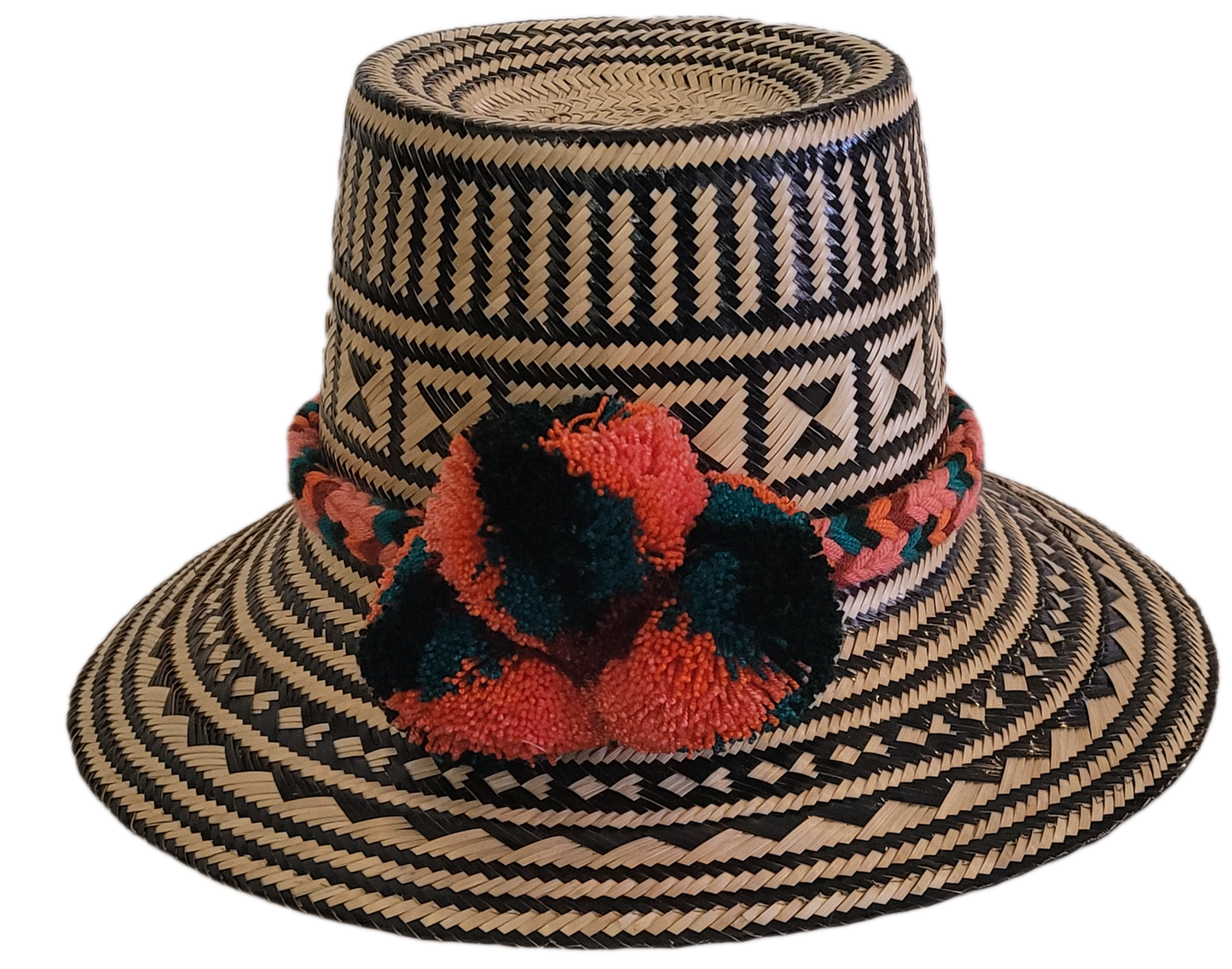 Handwoven black and natural Wayuu straw hat with bold geometric patterns and coral-green pompoms — boho artisan fashion for sunny days.