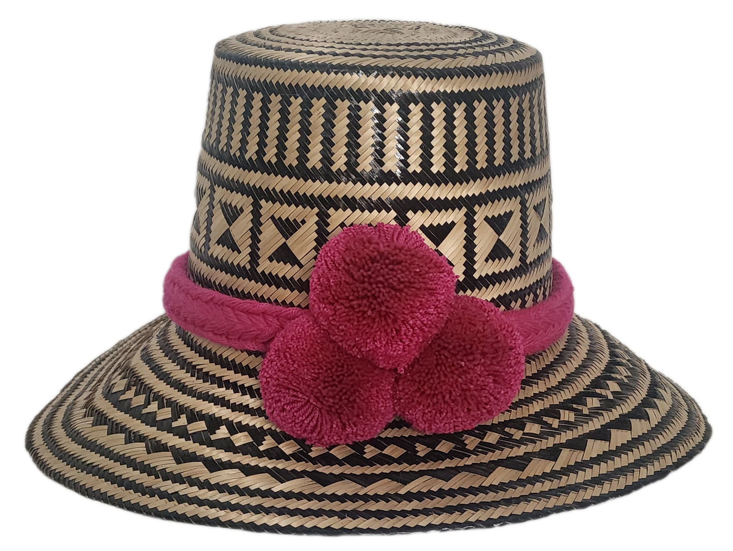 Handwoven Wayuu straw hat with black geometric patterns, vibrant pink braided band, and three matching handmade pink pom-poms.