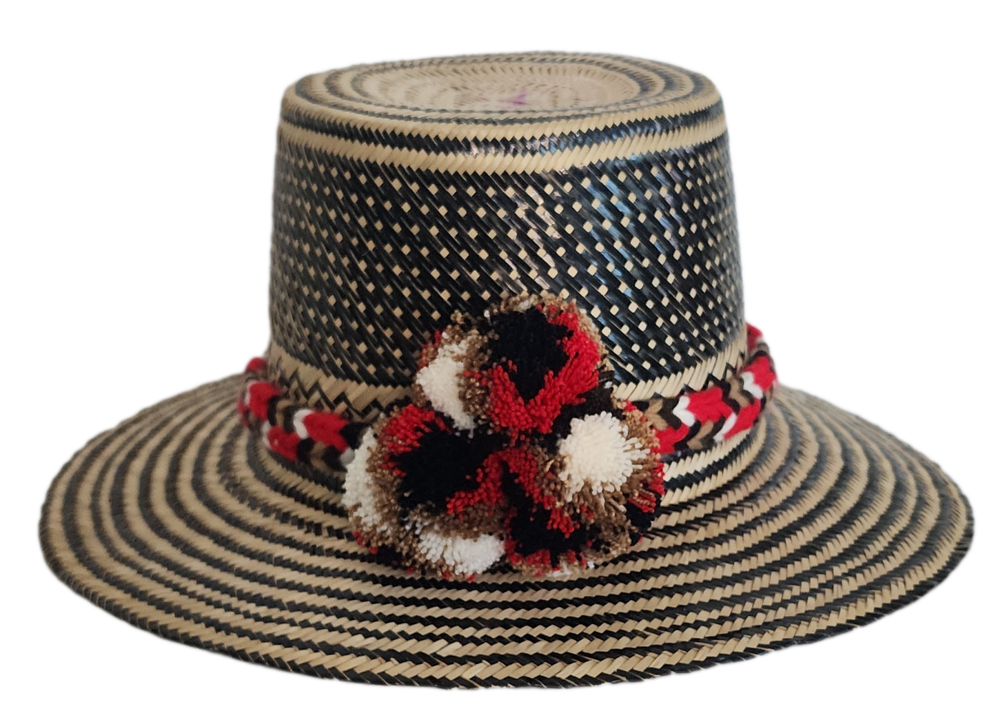 Colorful boho straw hat handwoven by Wayuu artisans, featuring a black and natural pattern, red-and-white braided band, and vibrant pom-poms — a bohemian fashion accessory perfect for summer.