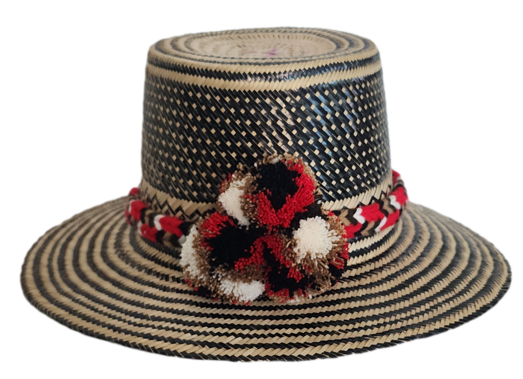 Colorful boho straw hat handwoven by Wayuu artisans, featuring a black and natural pattern, red-and-white braided band, and vibrant pom-poms — a bohemian fashion accessory perfect for summer.