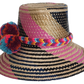 Boho Wayuu straw hat with vibrant pink, navy, and natural woven design, a multicolor braided band, and playful pom-poms in turquoise, red, and orange — a colorful, handcrafted bohemian summer accessory.