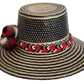 Colorful boho straw hat handwoven by Wayuu artisans, featuring a black and natural pattern, red-and-white braided band, and vibrant pom-poms — a bohemian fashion accessory perfect for summer.