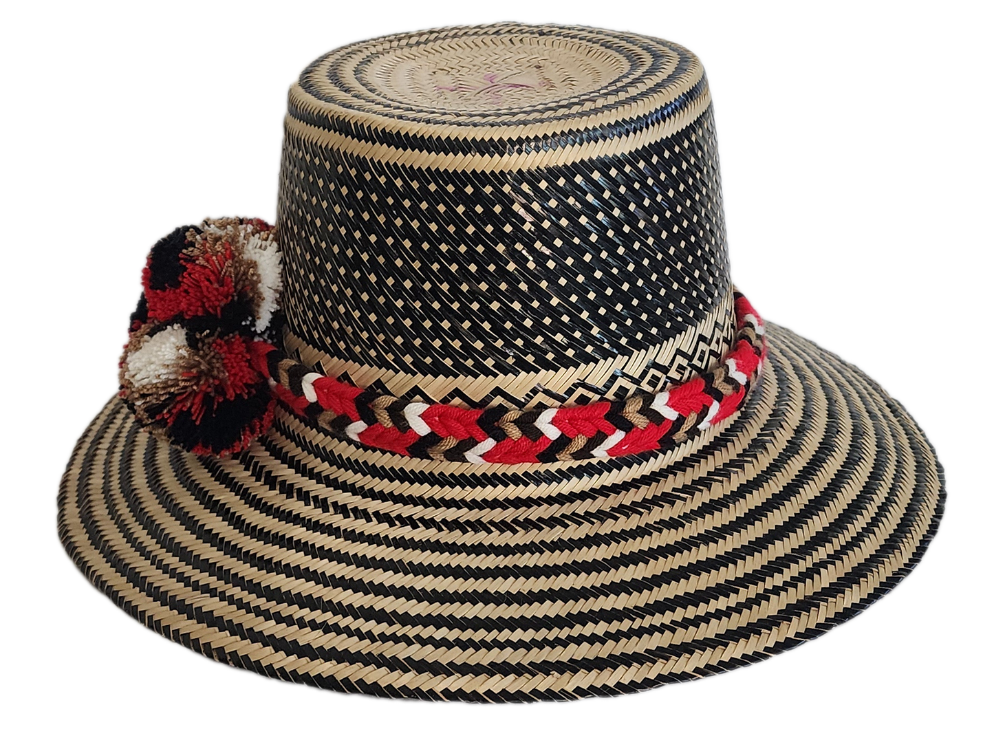 Colorful boho straw hat handwoven by Wayuu artisans, featuring a black and natural pattern, red-and-white braided band, and vibrant pom-poms — a bohemian fashion accessory perfect for summer.
