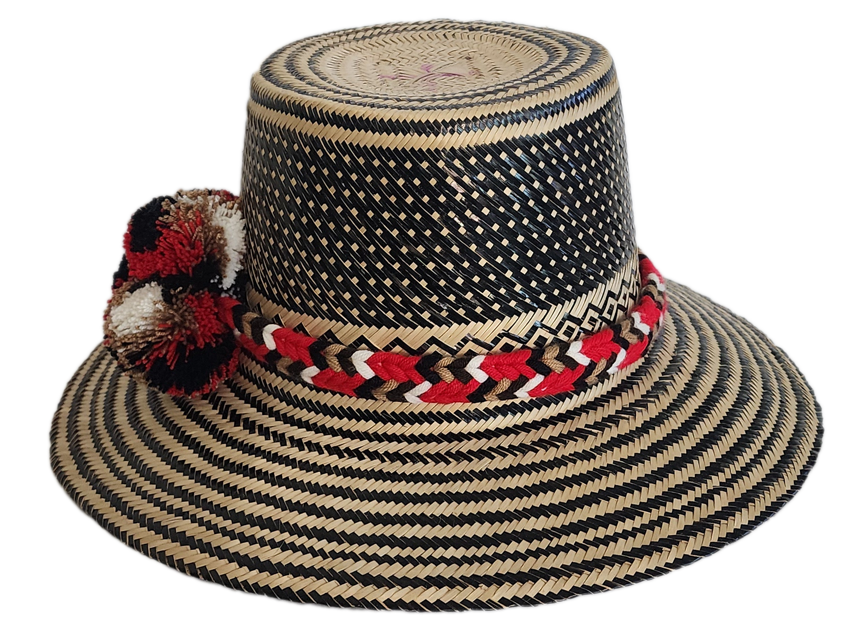 Colorful boho straw hat handwoven by Wayuu artisans, featuring a black and natural pattern, red-and-white braided band, and vibrant pom-poms — a bohemian fashion accessory perfect for summer.