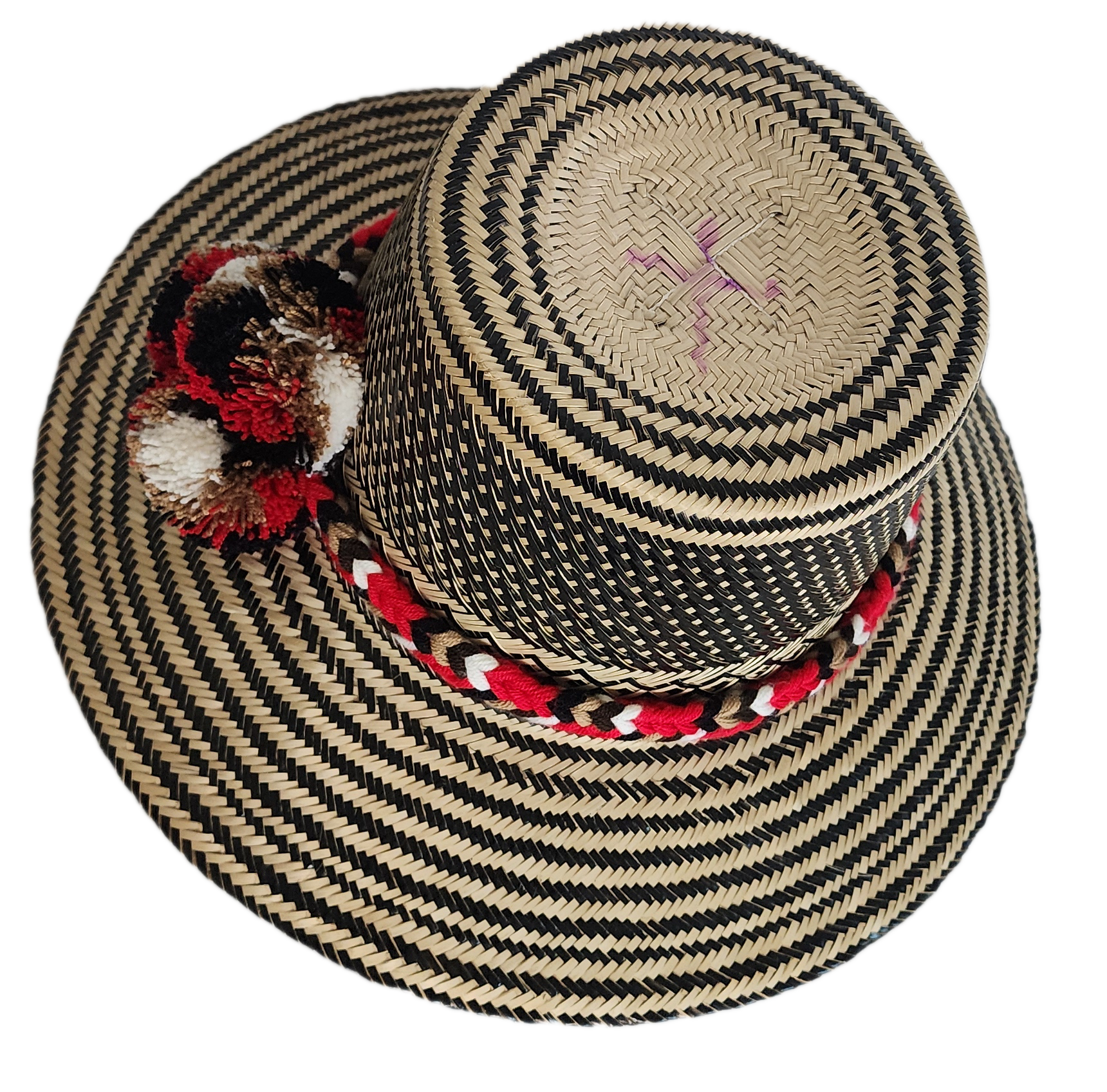 Colorful boho straw hat handwoven by Wayuu artisans, featuring a black and natural pattern, red-and-white braided band, and vibrant pom-poms — a bohemian fashion accessory perfect for summer.