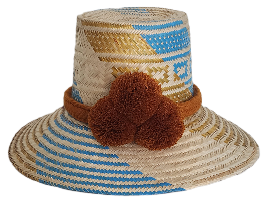 Handwoven Wayuu straw hat featuring blue and gold geometric patterns, a wide brim, and a brown braided band with three pom-pom accents in the front.