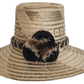 A stylish, handmade straw hat featuring intricate light and dark straw geometric patterns and a unique band with black, brown, and cream twisted elements and a black and brown pompom.