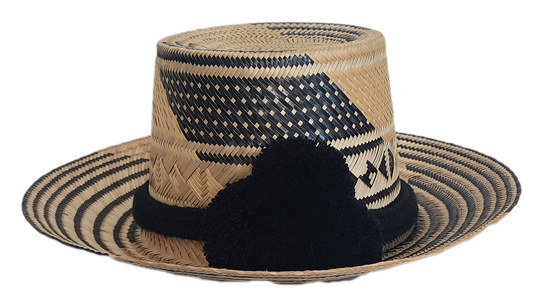 A stylish, handmade straw hat featuring intricate black and natural straw weaving patterns and a bold black pompom band.