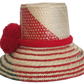 A vibrant, handmade straw hat featuring red and green geometric patterns and a bold red pompom band with three fluffy pompoms.