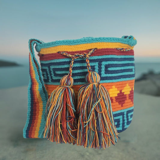 A vibrant, colorful crochet bag featuring a boho-Wayuu design. The item showcases intricate patterns typical of Bohemian and Wayuu style, with a rich mix of bright, eye-catching colors. Handmade, the bag exemplifies skilled crochet craftsmanship, ideal for adding a bohemian flair to any outfit.