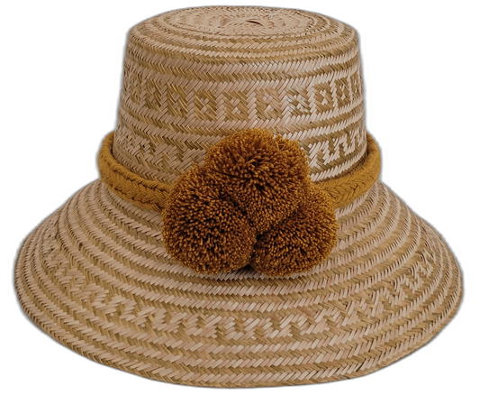 Handmade Wayuu straw hat in light natural tones with ochre pompoms.

