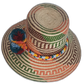 Wayuu artisan hat featuring woven rust and green patterns with bright pompom accents