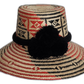 Handmade Wayuu straw hat with red and black geometric weave and black pompoms.Arya handmade Wayuu hat with red and black diamond pattern and black pompoms