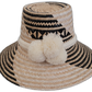 Handmade Wayuu bohemian straw hat with cream pompoms and black-beige woven patterns.


