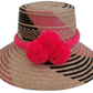 Handmade Wayuu straw hat with bold pink and black patterns, featuring large pink pompoms, perfect bohemian chic style.