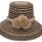 Handmade Wayuu straw hat featuring bold black and natural palm patterns with large pompoms

