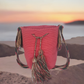 Handmade Wayuu crochet bag in solid pink with long multicolor tassels and a wide artisan strap — a vibrant boho-chic statement piece.