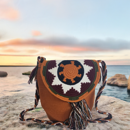 Handmade Wayuu crochet flap bag in burnt orange with tribal sun design and multicolor tassels — artisan boho-chic piece with earthy tones.